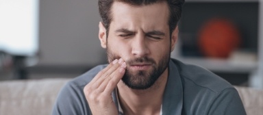 Man in need of emergency dentistry holding cheek in pain