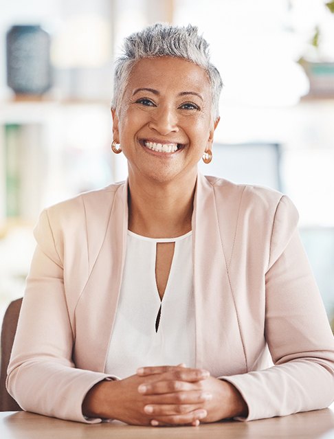 Senior woman smiling and sitting at table with hands folded