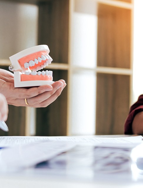 Hands holding model teeth at desk with X-rays