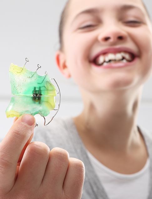 Young girl holding up a multi colored retainer