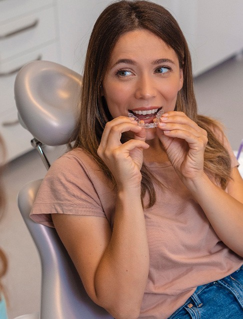 Female dental patient looking at dentist and putting in clear aligner