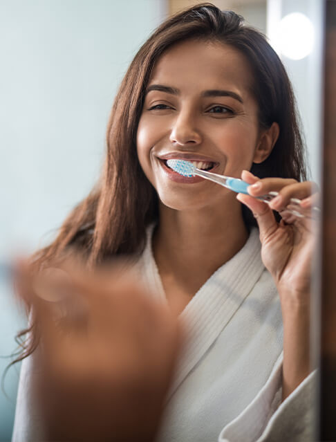 young woman brushing teeth in bathroom mirror