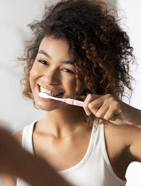 young woman brushing teeth in bathroom mirror