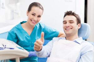 Dentist and patient smiling with patient giving thumbs-up.